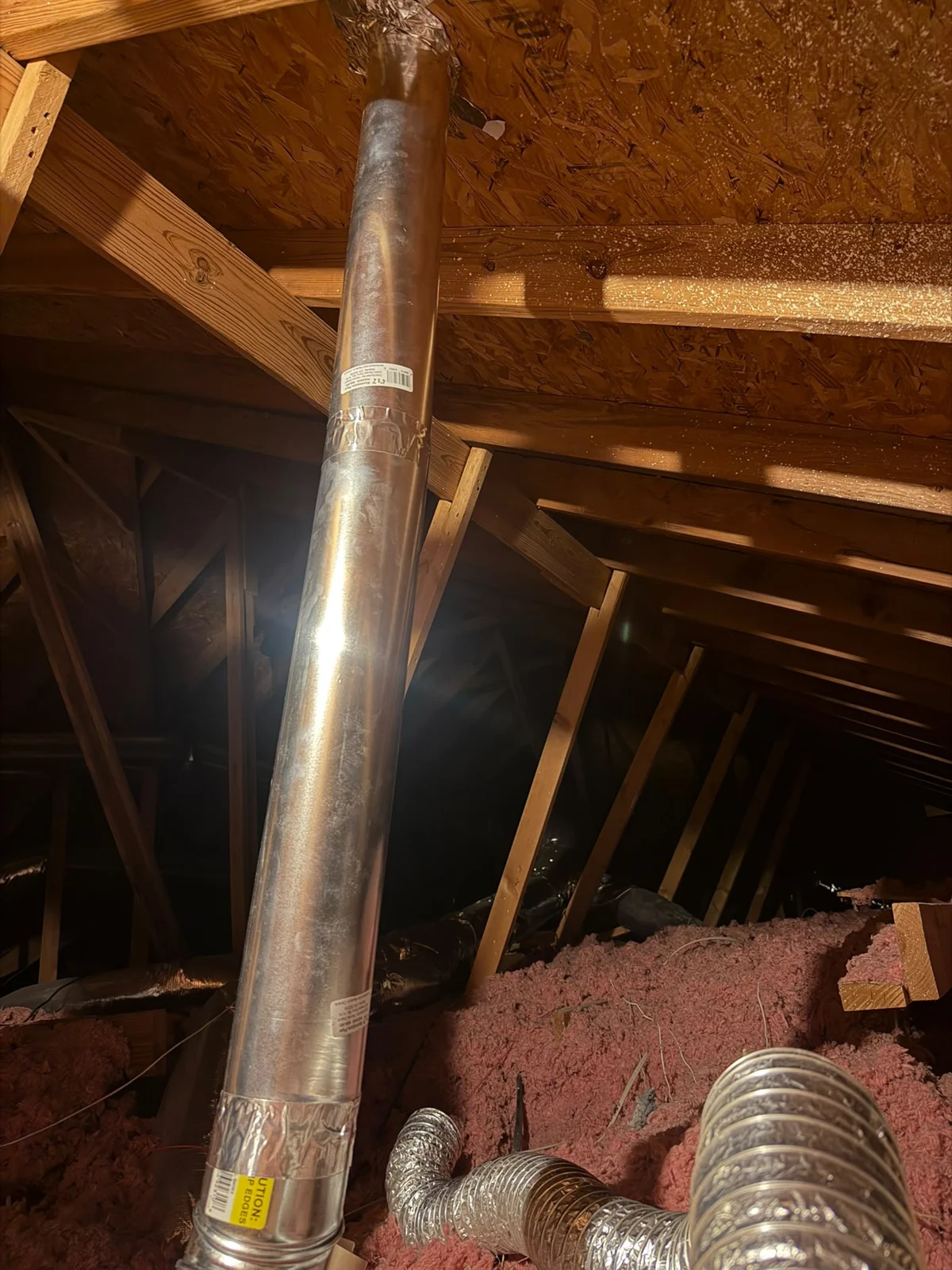 Client photograph of the matching attic area with a rigid metal vent pipe