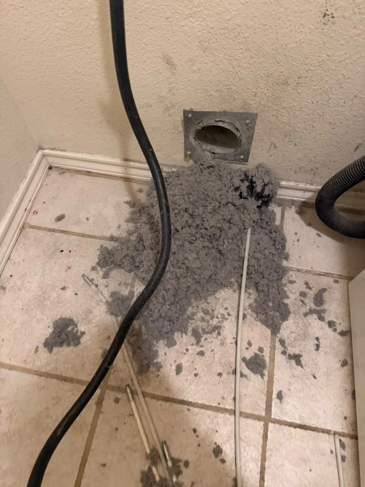 Client photograph of lint and debris below an open dryer wall connection during work